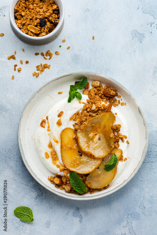 Wall mural Greek yogurt with caramelized pear, granola, nuts and melted sugar for a wholesome breakfast on a gray ceramic plate. Rustic style. Top view. - Wall murals