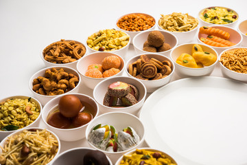 Rangoli of sweets and Farsan/snacks in bowls for Diwali with diya over white background