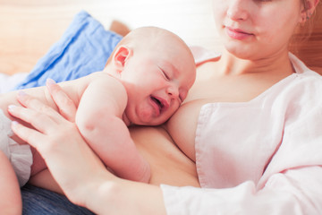 Crying newborn baby on mothers breasts while breastfeeding