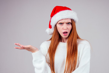 Fototapeta na wymiar thoughtful beautiful redhaired ginger woman wearing white knitted sweater and santa claus hat choosing amd thinking studio background