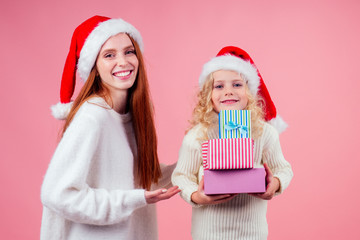 getting xmas presents.girls in red santa hat holding a bunch of gifts boxes in studio pink background