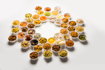 Rangoli of sweets and Farsan/snacks in bowls for Diwali with diya over white background