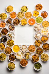 Rangoli of sweets and Farsan/snacks in bowls for Diwali with diya over white background