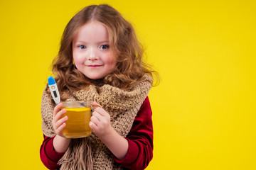 sick illness little blonge girl wearing knitted scarf and drinking hot tea cup with lemon and ginger in studio yellow background