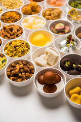 Rangoli of sweets and Farsan/snacks in bowls for Diwali with diya over white background