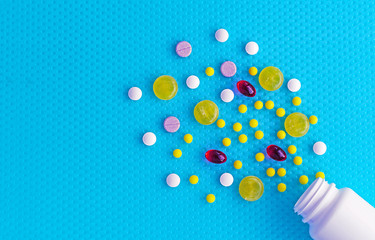White bottle and multi-colored pills with medicines on a blue background. Medicine concept.