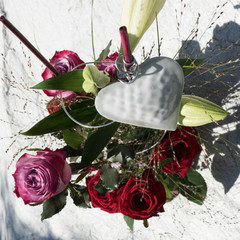 White heart on a floral bouquet surrounded by a variety of roses, Deep Purple and Red Naomi, and green leaves.