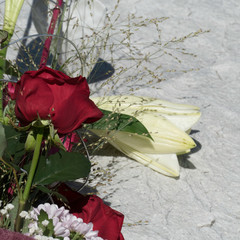 Detail of flower bouquet with red roses, grasses, green leaves, Lilium Longiflorum, Gypsophila and Chrysanthemum Santini placed on a stony backdrop.