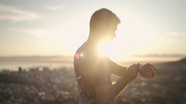 Young male athlete listening to music during workout adjusting smart watch before jogging on mountain top at early morning - male runner getting ready for the run