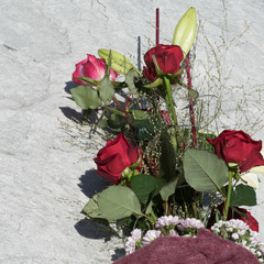 Flower bouquet in a violet sleeve with a variety of roses, green leaves, Lilium Longiflorum, Gypsophila and Chrysanthemum Santini placed on a stony background. Copy space at the side.