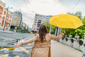 Fototapeta premium Joyful woman walking in rainy weather. Happy young woman walking with umbrella under the rain. I love it when it's raining! This weather won't get me down