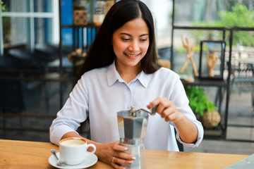Asian woman drinking coffee with coffee grinder in cafe