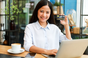 Asian woman using credit card shopping online in coffee shop cafe