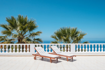 two sun beds on villa terrace with ocean and palm tree background