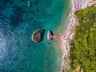 Aerial view of Sveti Nicola, Budva island, Montenegro. Hawaii beach, umbrellas and bathers and crystal clear waters. Jagged coasts