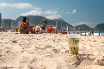 Caipirinha con lima limón, bebida tradicional, en la playa de Río de Janeiro con muchachas atrás