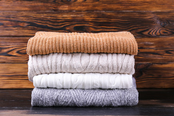 Obraz na płótnie Canvas Bunch of knitted pastel color sweaters with different knitting patterns perfectly folded in stack on brown wooden table, wood textured background. Fall winter season knitwear. Close up, copy space.