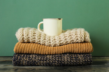 Bunch of knitted pastel color sweaters with different knitting patterns perfectly folded in stack on brown wooden table, green textured background. Fall winter season knitwear. Close up, copy space.