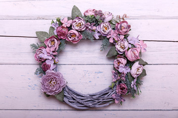 Door wreath made of artificial flowers and autumn plants on shabi white wooden background.