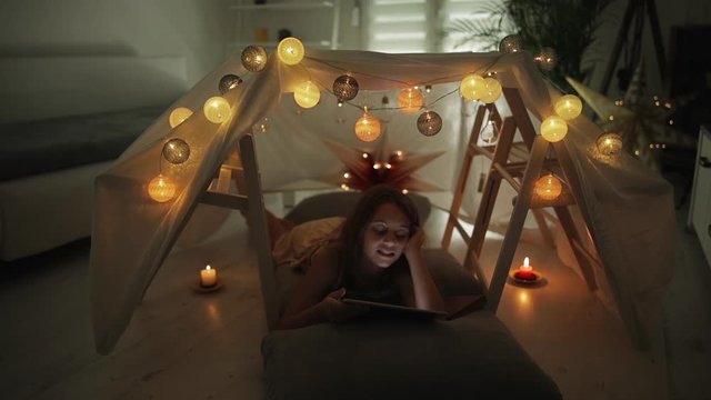 Little 10 year old girl using tablet under her home-made tent inside the living room.