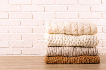 Obraz na płótnie Canvas Bunch of knitted pastel color sweaters with different knitting patterns perfectly folded in stack on brown wooden table, white brick wall background. Fall winter season knitwear. Close up, copy space.