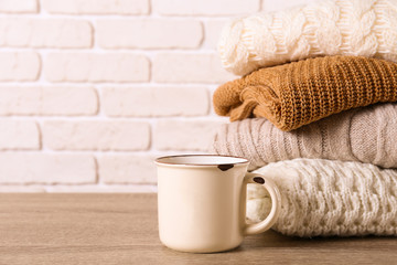 Bunch of knitted pastel color sweaters with different knitting patterns perfectly folded in stack on brown wooden table, white brick wall background. Fall winter season knitwear. Close up, copy space.