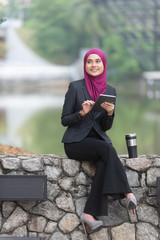 Obraz premium Muslim Businesswoman with her tablet and her coffee at the park.
