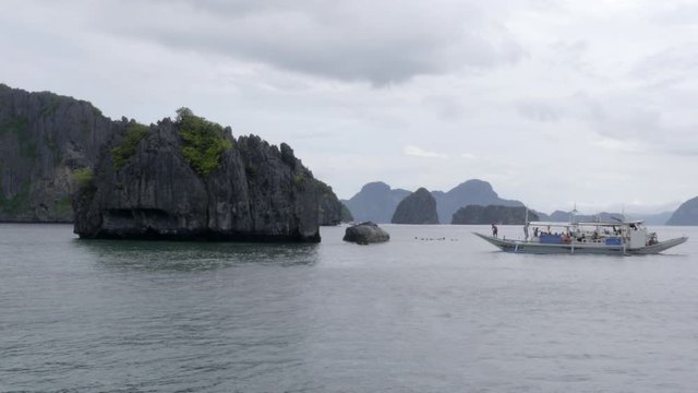 Longboat sailing in the bay of Palawan, rocky islands in the sea on cloudy day.