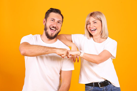 Young beautiful hipster couple having fun posing over isolated yellow background. Portrait of tall man with groomed beard and his short attractive blonde girlfriend. Copy space, close up.