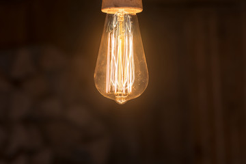 Vintage incandescent lamp shines with warm light. Edison lamp on on a dark background.
