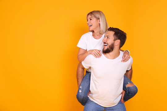 Young Beautiful Hipster Couple Having Fun Posing Over Isolated Yellow Background. Portrait Of Tall Man With Groomed Beard And His Short Attractive Blonde Girlfriend. Copy Space, Close Up.