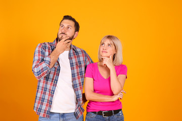 Young beautiful hipster couple having fun posing over isolated yellow background. Portrait of tall man with groomed beard and his short attractive blonde girlfriend. Copy space, close up.