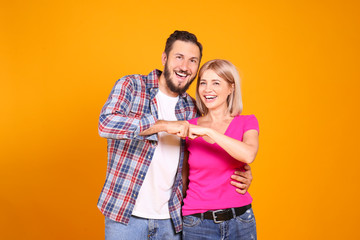 Young beautiful hipster couple having fun posing over isolated yellow background. Portrait of tall man with groomed beard and his short attractive blonde girlfriend. Copy space, close up.