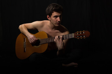 Obraz premium Handsome young musician playing on guitar. Naked torso. On black background.