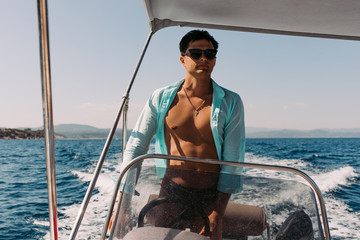 Man in sunglasses driving and navigating yacht in the sea. Sailing man on yacht in ocean