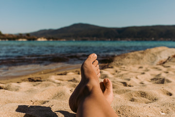 legs of a young woman lying on the beach on sunny summer day. Woman's feet relaxing on the beach.