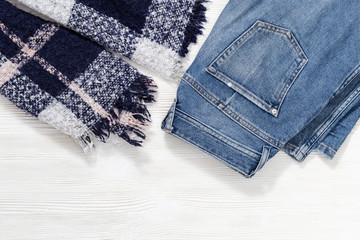 Autumn comfortable clothes. Warm cozy scarf, blue denim jeans on white wooden background. Female clothing. Casual fashion outfits. Flat lay. Top View.