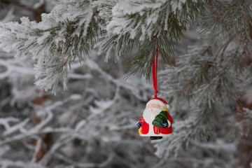 New Year. Christmas and decorations. Toy Santa Claus swinging on a branch in the forest. Snowing