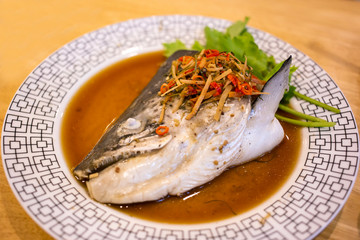Salmon kabutoni (Salmon head streamed with soy sauce, herbs, ginger, and vegetables in white dish at asian food restaurant.