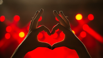 Girl showing heart-shape symbol enjoying her favorite group on the concert