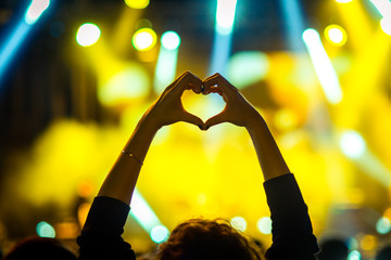 Girl showing heart-shape symbol enjoying her favorite group on the concert