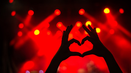 Girl showing heart-shape symbol enjoying her favorite group on the concert