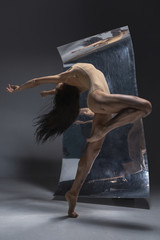 Young and stylish modern ballet dancer on grey background with the mirror and illusion reflections...