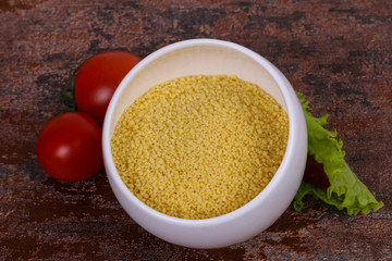 Raw couscous in the bowl served salad leaves, tomato and pepper