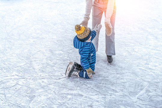 Mom with baby boy 3-5 years old, learn train, ride winter city rink, ice skating. The child gets up, fell on skates, kneels, play fun rest on weekend first steps child skates. Free space for text.