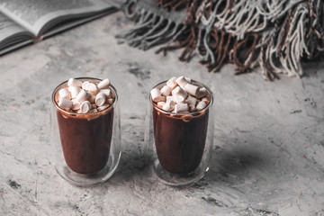 Two glasses of hot cocoa with marshmallow on the background of an open book and a woolen blanket