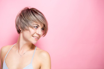 Portrait of young romantic woman with tender smile wearing casual outfit in pastel colors over pink background	