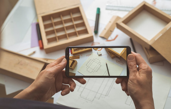 The designer of cardboard packaging takes pictures of the project sketches for a smartphone blog. The developer of paper boxes takes pictures on a mobile phone. 
