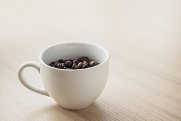 fresh roasted coffee beans in white cup on wood table