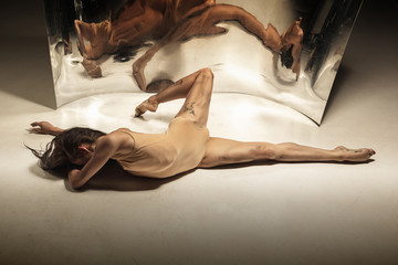Inspired. Young, stylish modern ballet dancer on brown background with mirror, illusion reflections...